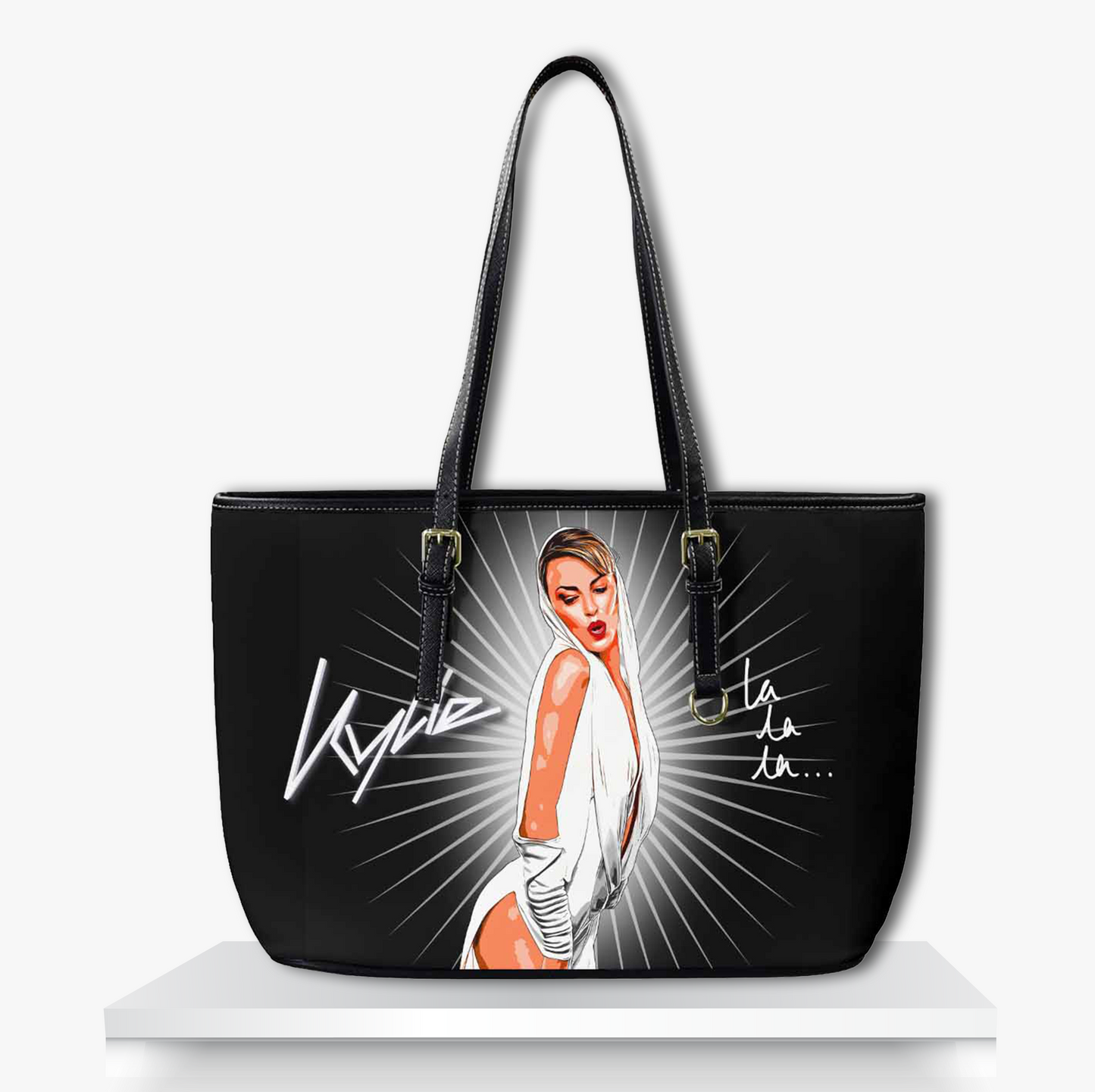 Black tote bag featuring a bold illustrated portrait of pop icon Kylie in a glamorous white outfit with radiant light beams, her signature and 'la la la…' lyric stylish music-inspired fashion accessory perfect for Kylie Minogue fans, dance-pop lovers, and statement style enthusiasts.