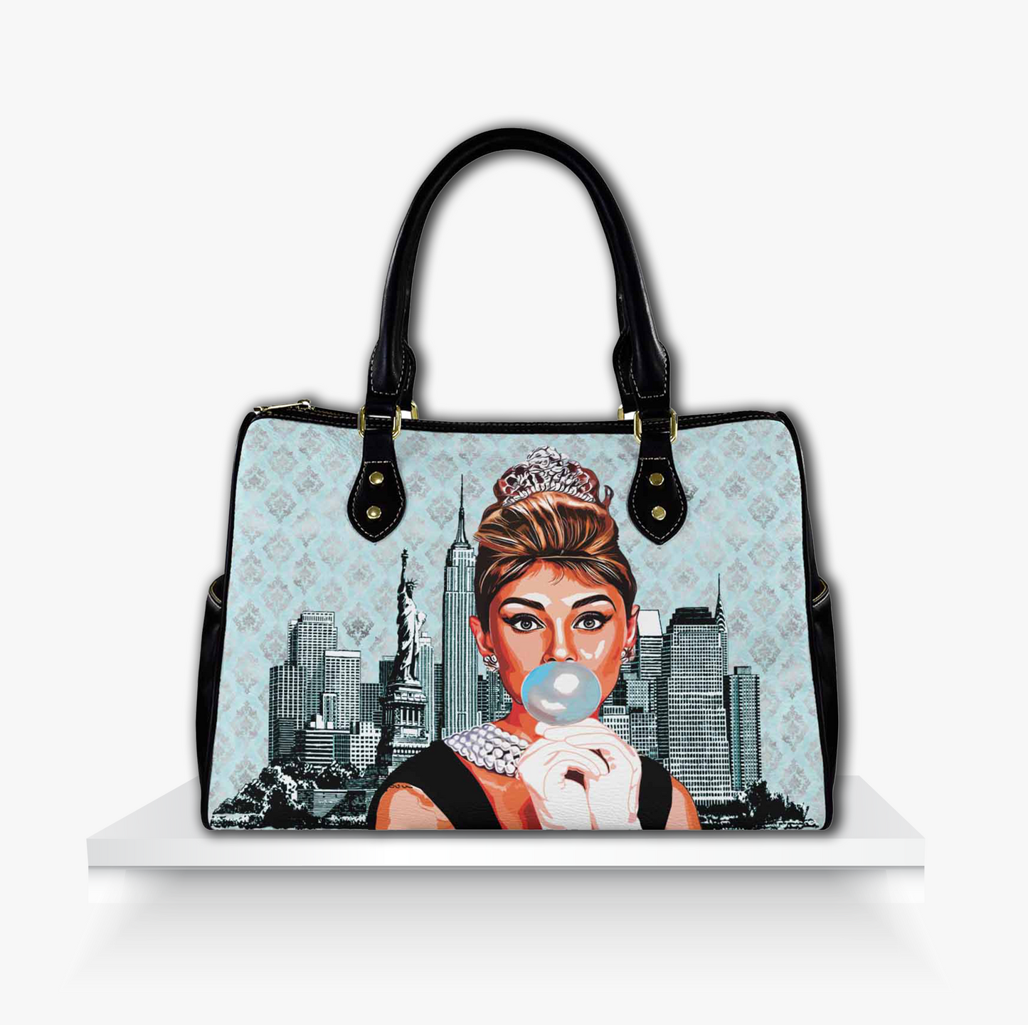 Light blue barrel-style handbag featuring a playful illustrated portrait of a woman styled like Audrey Hepburn blowing bubble gum, wearing a tiara and pearls, set against a vintage damask background and New York City skyline chic retro accessory perfect for fans of classic Hollywood glam and pop art fashion.