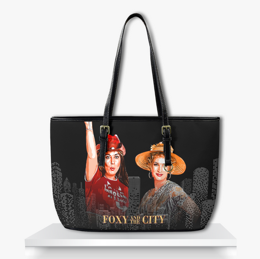 Stylish black tote bag with illustrated city skyline design featuring two fashionable women in bold outfits and hats, with gold text 'Foxy and the City' trendy urban fashion accessory for women, perfect for casual or statement looks.